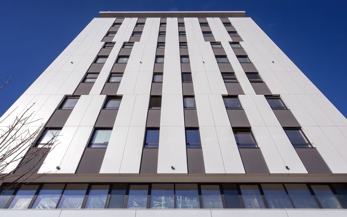 Stambena zgrada kompleksa 5 na Novom Beogradu sa belo-sivim zidovima i pravilno raspoređenim prozorima viđen sa tla.